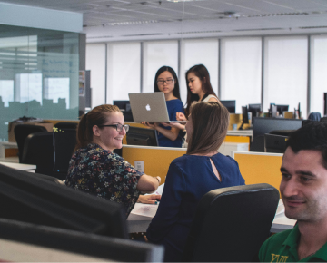 People working in an office with computers and desks having a meeting